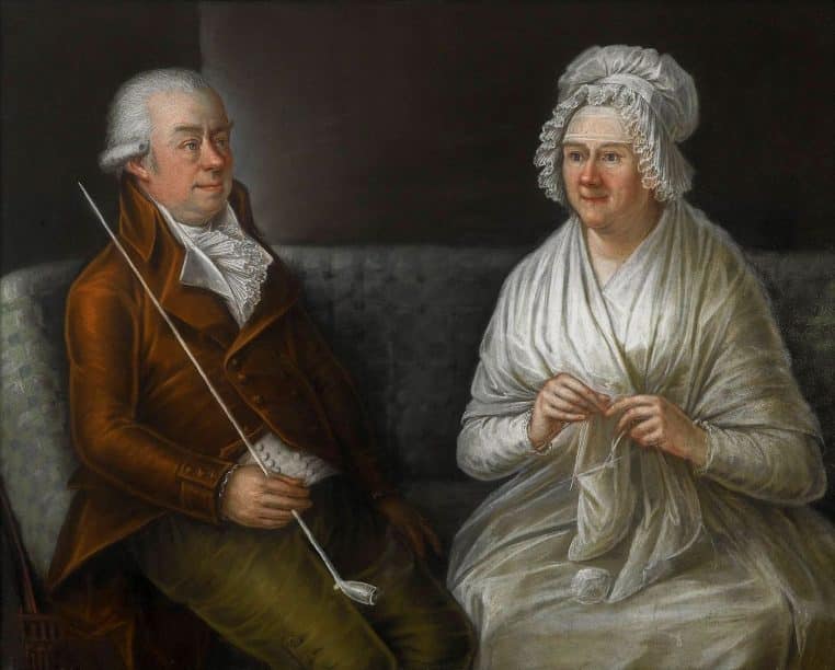 Portrait d’un couple de personnes âgées assis côte à côte sur un canapé, échangeant un moment calme dans un salon éclairé