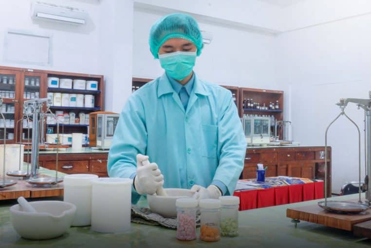 Assistant en blouse et masque préparant un mélange au mortier, flacons et matériel sur paillasse