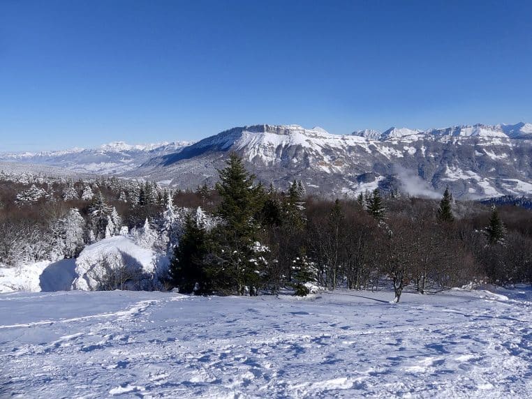 Vue panoramique depuis le Nivolet sur le massif des Bauges et le Mont-Blanc après des chutes de neige, avec forêt enneigée au premier plan et ciel dégagé.