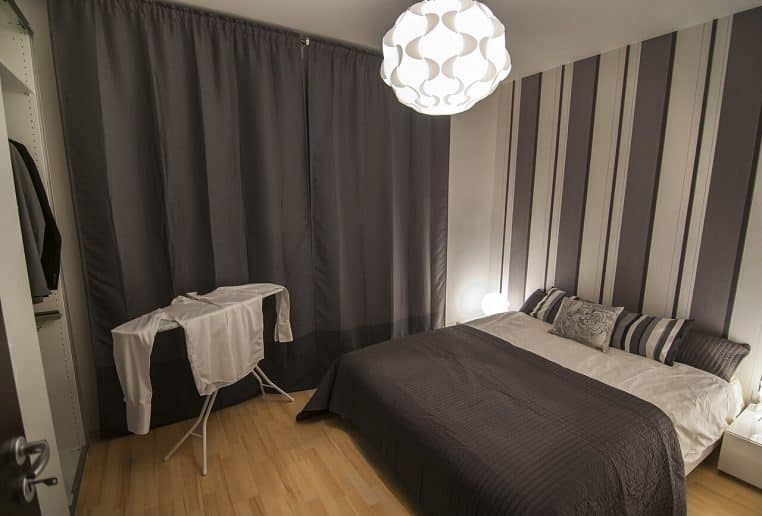 Grande chambre lumineuse avec lit double recouvert de linge clair, vue sur une baie vitrée donnant sur le paysage extérieur marin.