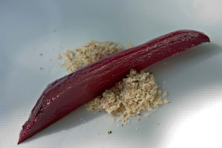 Long bâtonnet de betterave rôtie posé sur un lit de sel assaisonné, présenté sur une assiette blanche minimaliste.