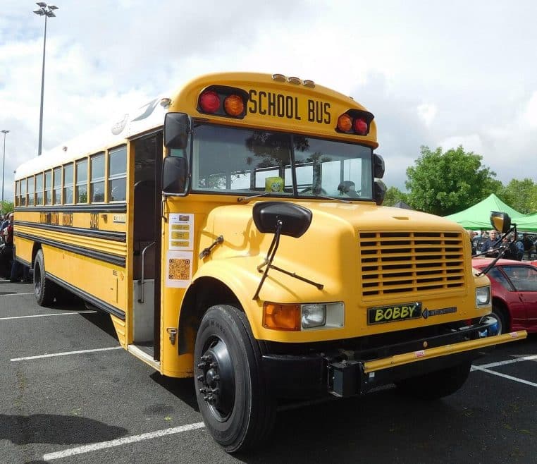 Ancien bus scolaire jaune stationné sur un terrain en Dordogne, photographié de côté en plan large.