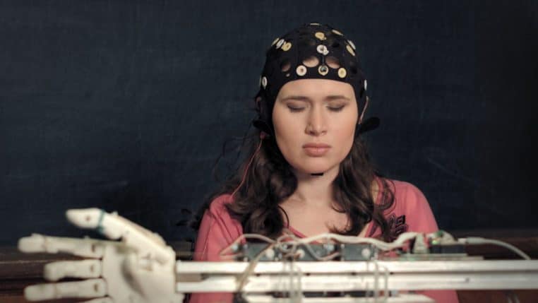 Une jeune femme coiffée d’un bonnet d’électrodes colorées est assise devant un écran dans un laboratoire de recherche en neurosciences.