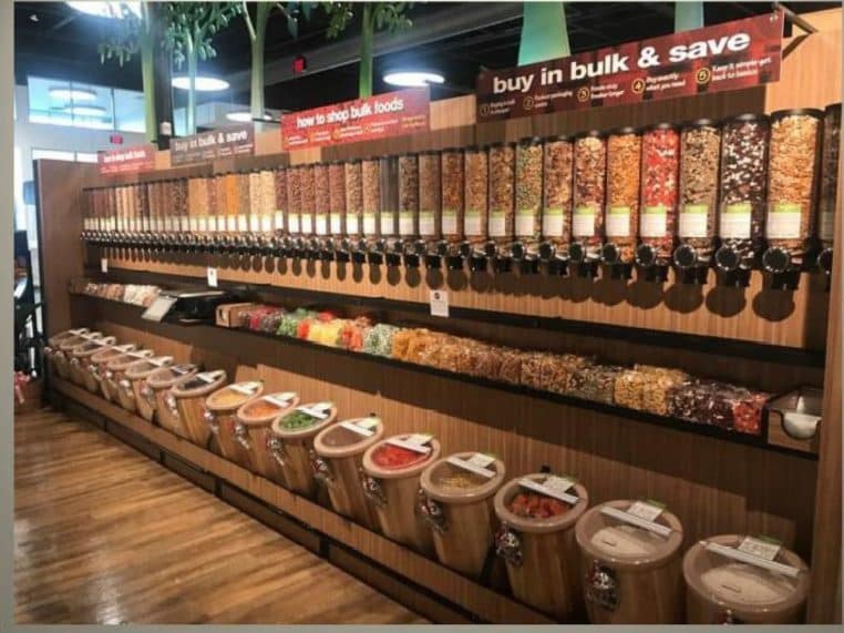 Mur de distributeurs de produits en vrac dans un magasin, avec bocaux et silos alignés sur une allée en bois