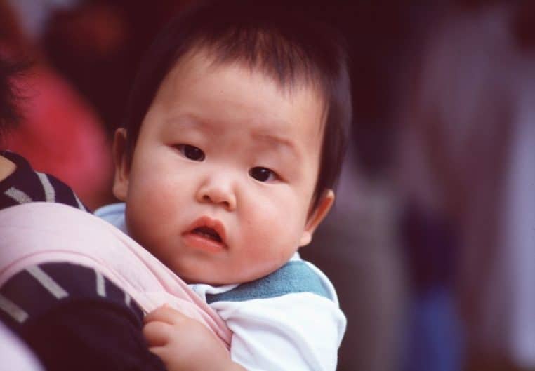 Enfant porté sur le dos de sa mère, image de proximité et de protection, dans un décor du quotidien.