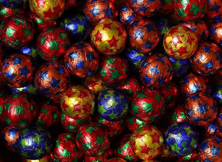Gros plan horizontal sur des chocolats de Noël emballés dans des papiers colorés, évoquant les assortiments festifs des rayons saisonniers.