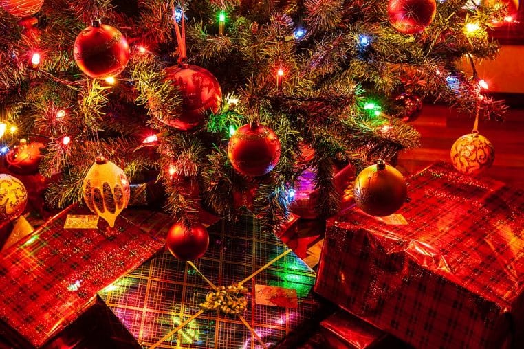 Sapin de Noël décoré dans un salon, entouré de nombreux cadeaux emballés et alignés au pied de l’arbre.