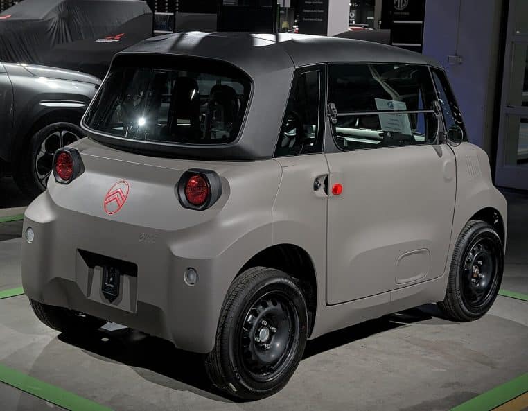 Citroën Ami exposée dans un salon automobile en 2025, éclairage de stand et visiteurs autour, soulignant son positionnement de micro-voiture électrique urbaine.