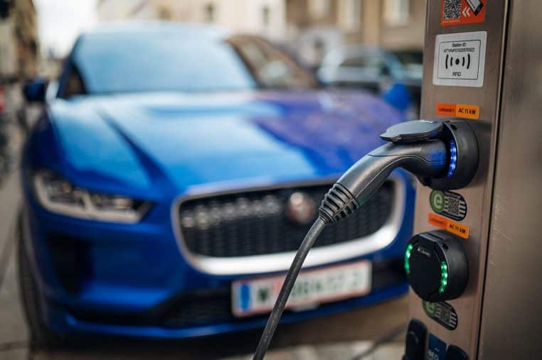 Gros plan sur la prise d’une borne de recharge rapide pour voiture électrique, avec un véhicule flou à l’arrière-plan.