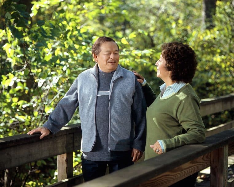 Couple de seniors marchant sur une passerelle en bois en pleine nature, discutant calmement de leur avenir et de leur retraite complémentaire.