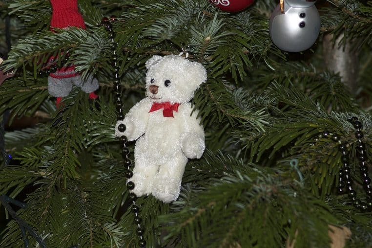 Gros plan sur des décorations rouges et dorées suspendues à un sapin de Noël naturel, avec des lumières floues en arrière-plan.