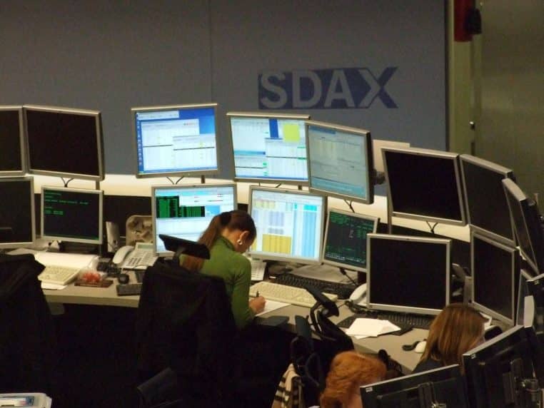 Salle de trading avec de multiples écrans et une opératrice au poste, ambiance marché financier.