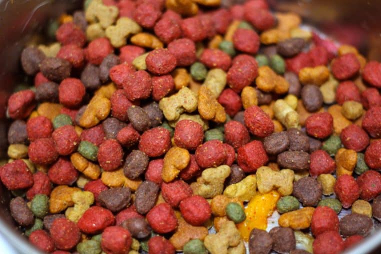 Mélange coloré de croquettes pour chien dans une gamelle en métal, avec différentes formes et couleurs illustrant la variété des produits.