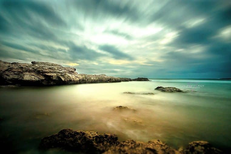 Ciel chargé et mer méditerranéenne devant des rochers, effet longue exposition et atmosphère de temps perturbé.