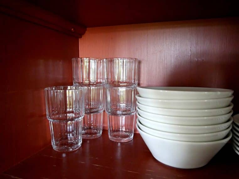Verres alignés et assiettes empilées dans un placard de cuisine, portes ouvertes laissant voir l’organisation des étagères