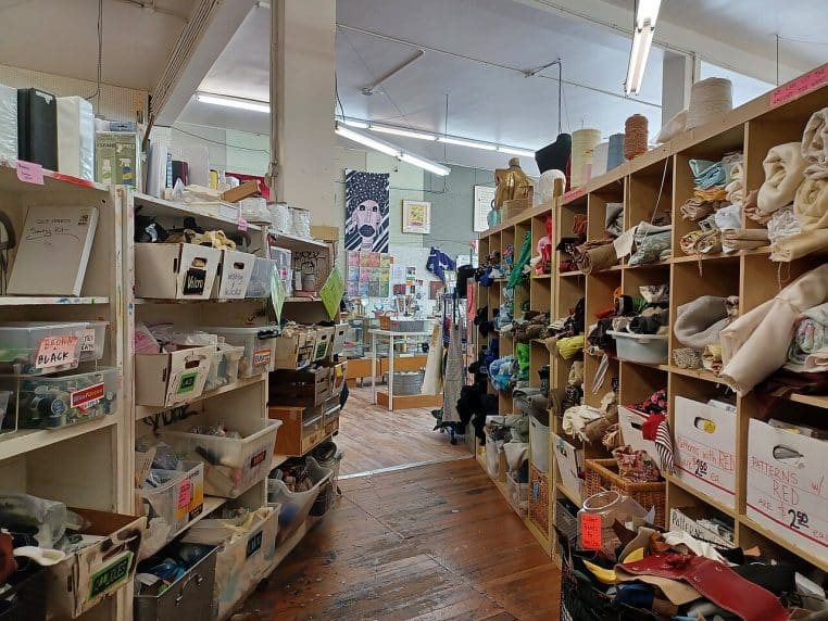 Allée d’un magasin associatif avec bacs et étagères, atmosphère de “chiner” et de fouille méthodique.
