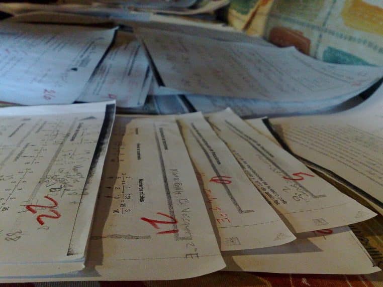 Pile de copies d’examen annotées au stylo rouge, chiffres entourés et remarques visibles, posées en désordre sur une table après correction, symbolisant la sélection des candidats.