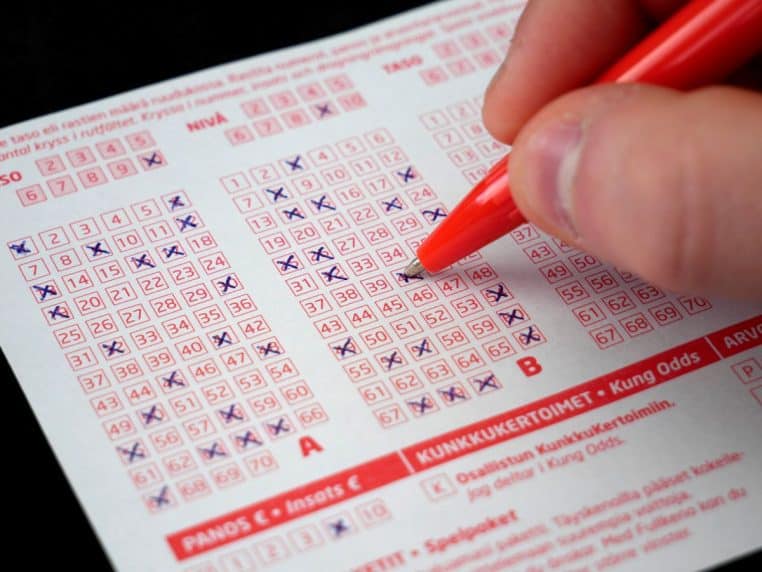 Main cochant une grille de keno au stylo rouge, ticket de loterie en gros plan sur une table sombre.