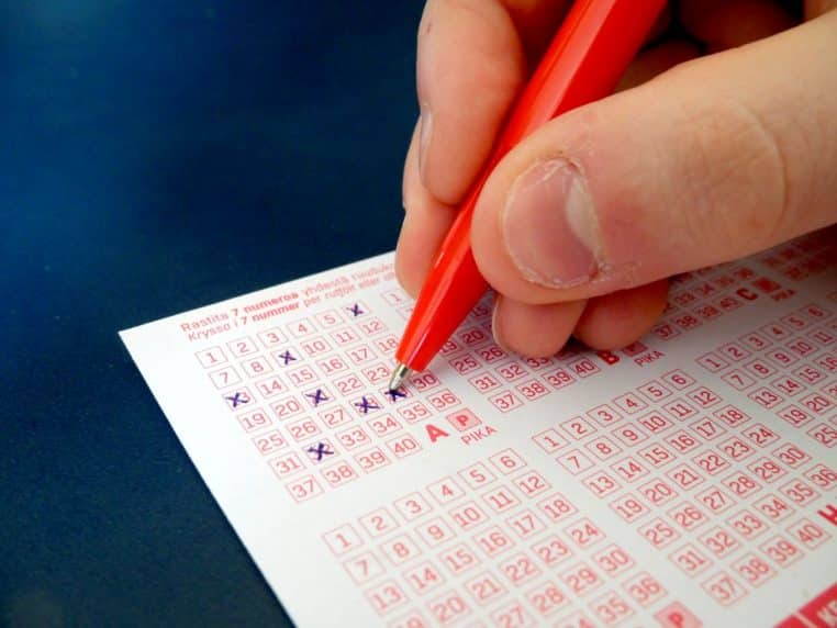 Main remplissant une grille de ticket de loterie, crayon et cases numérotées, scène typique avant un tirage.