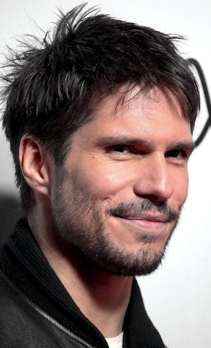 François Civil de trois-quarts, en gros plan, pose face aux photographes lors d’une projection de L’Amour Ouf en 2024, éclairé par les spots du tapis rouge