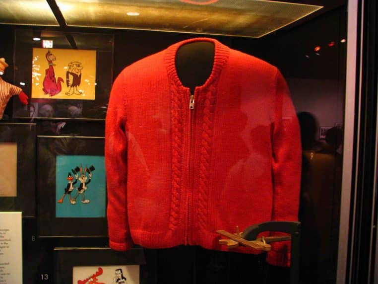 Pull rouge en maille exposé dans une vitrine de musée, symbole d’un vêtement iconique à la fois simple, chaud et rassurant.