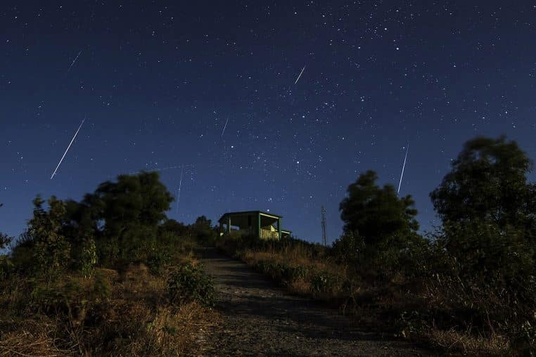 Ciel nocturne strié de météores des Géminides au-dessus d’un sentier et d’une petite cabane, en hiver.