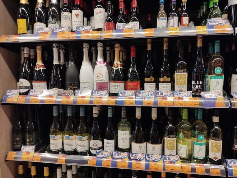Rangées de bouteilles de vin en rayon de supermarché, étiquettes visibles et éclairage de magasin, photo paysage.