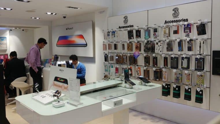 Intérieur de boutique de smartphones avec mur d’accessoires, comptoir vitré et clients, éclairage blanc uniforme