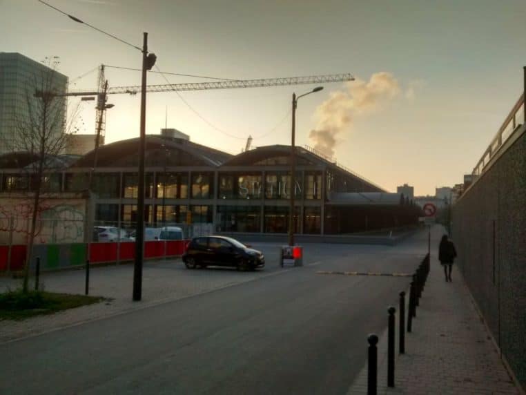 Vue extérieure de la Halle Freyssinet abritant Station F au crépuscule, avec grues, voitures garées et silhouette du bâtiment vitré.