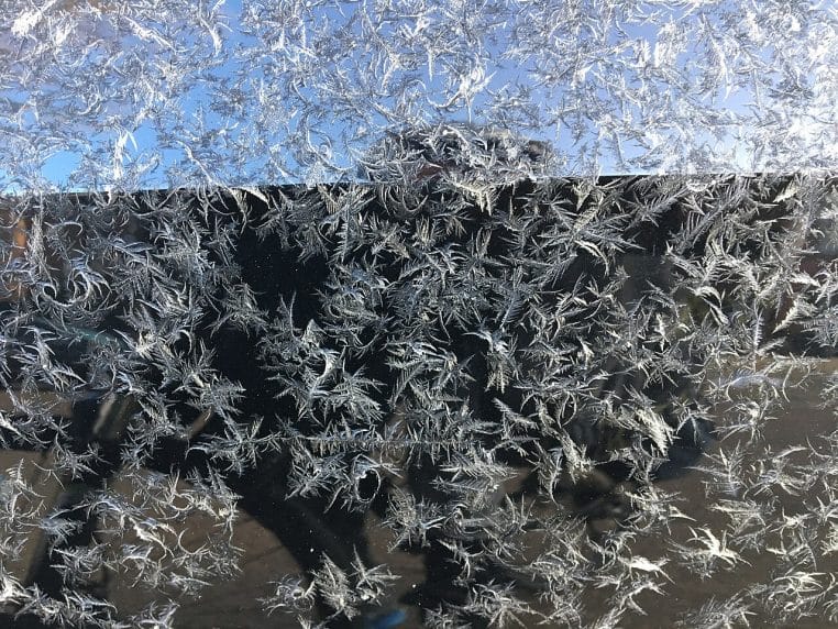 Cristaux de givre sur une vitre de voiture au petit matin, motifs étoilés et lumière froide d’hiver.