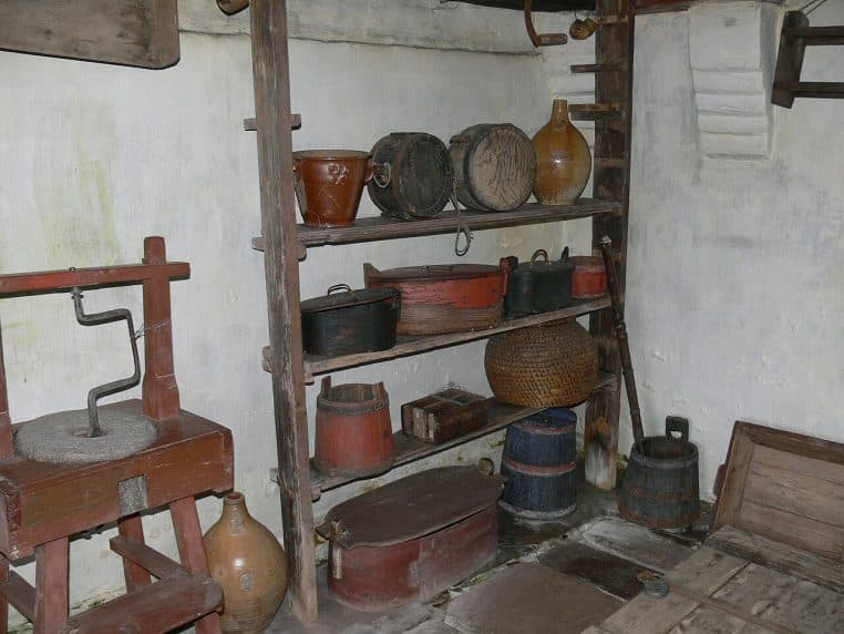 Anciennes étagères de cuisine en bois remplies de casseroles, bols et récipients, illustrant un rangement rustique de la vaisselle