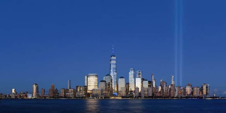 Panorama nocturne de Lower Manhattan vu depuis Jersey City, gratte-ciel illuminés et rivière au premier plan.