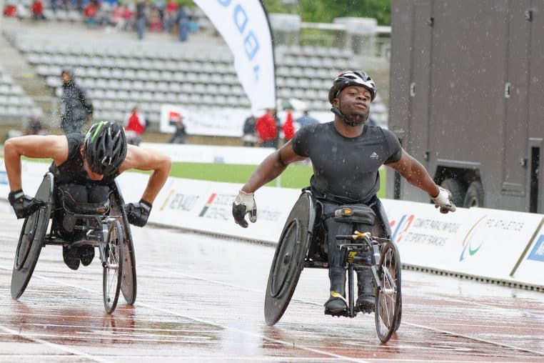 Deux athlètes en fauteuil roulant franchissant la ligne lors d’une course sous la pluie au Meeting d’athlétisme paralympique de Paris.