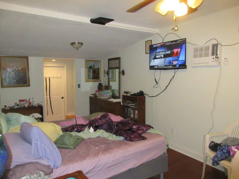 Chambre en désordre avec vêtements, sacs et objets au sol, lumière naturelle, ambiance de chaos quotidien