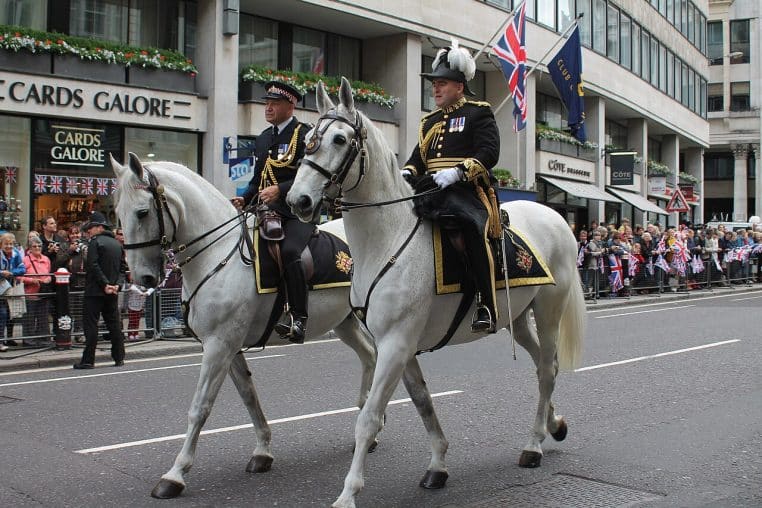 Deux policiers à cheval défilent dans une rue de Londres, foule en arrière-plan, scène urbaine en journée