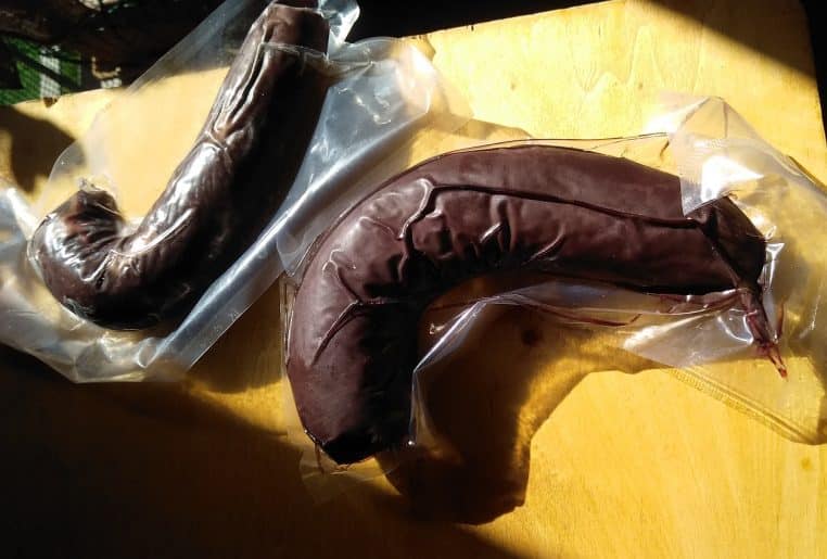 Deux saucisses traditionnelles emballées sous vide dans des sachets transparents, posées sur une planche en bois jaune.