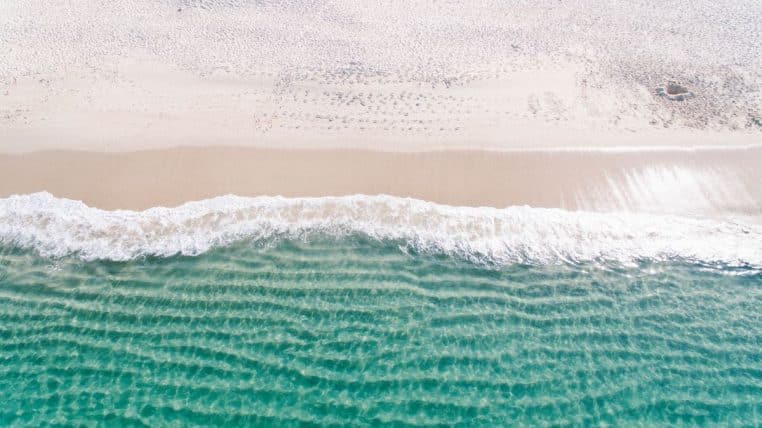 Vue aérienne de vagues turquoise venant mourir sur une plage de sable clair, photographiées par un drone au-dessus de l’océan.