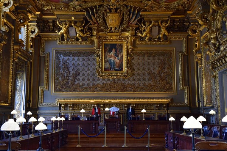 Salle d’audience de la Cour de cassation à Paris, boiseries dorées, pupitres et lampes alignées.