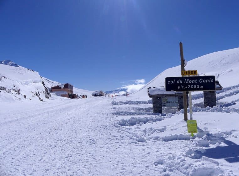 Panneau routier du col du Mont-Cenis à 2 083 mètres entouré de neige abondante, sous un ciel bleu limpide en plein hiver savoyard.