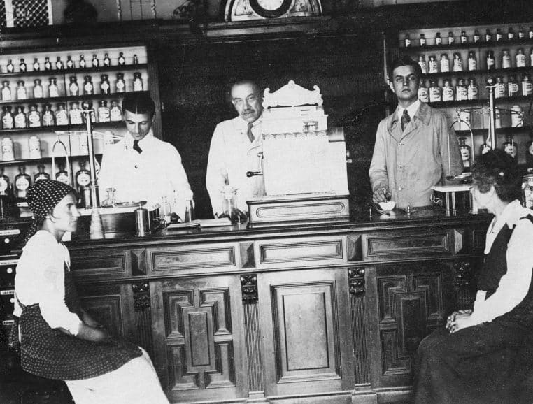 Photo d’archive d’une pharmacie ancienne avec comptoir en bois, flacons au mur et balance, scène en noir et blanc