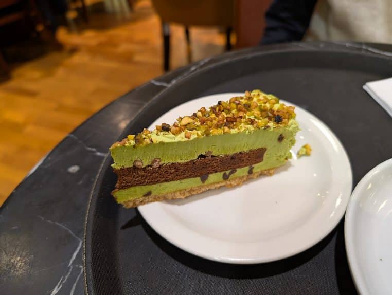 Gâteau mousse au chocolat et pistache servi sur une assiette de café, nappé de chantilly, évoquant une bûche de Noël gourmande.