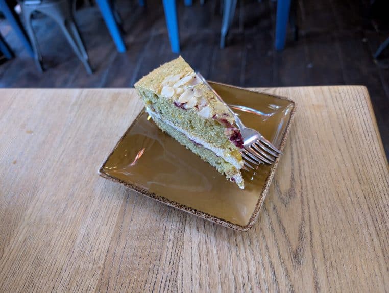 Tranche de gâteau pistache, framboise et amande joliment dressée sur une assiette, rappelant une bûche de Noël pâtissière raffinée.