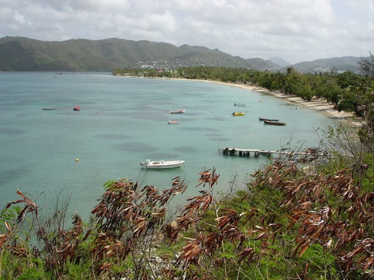 Panorama d’une plage à Sainte-Anne en Martinique, mer turquoise, barques au mouillage et collines au loin.