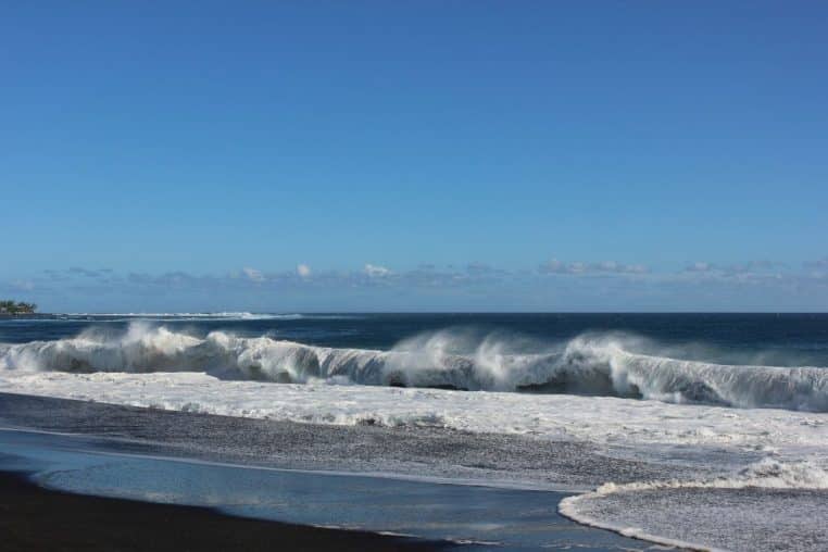 Vue de la plage de l’Étang-Salé à La Réunion, sable sombre, filaos et mer ouverte sous un ciel lumineux.