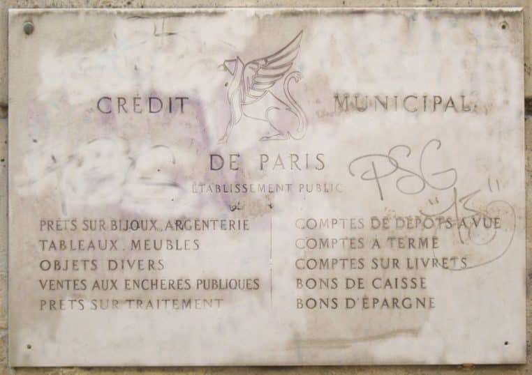Plaque en pierre du Crédit Municipal de Paris détaillant les types de prêts et comptes proposés, fixée sur un mur marqué par le temps.