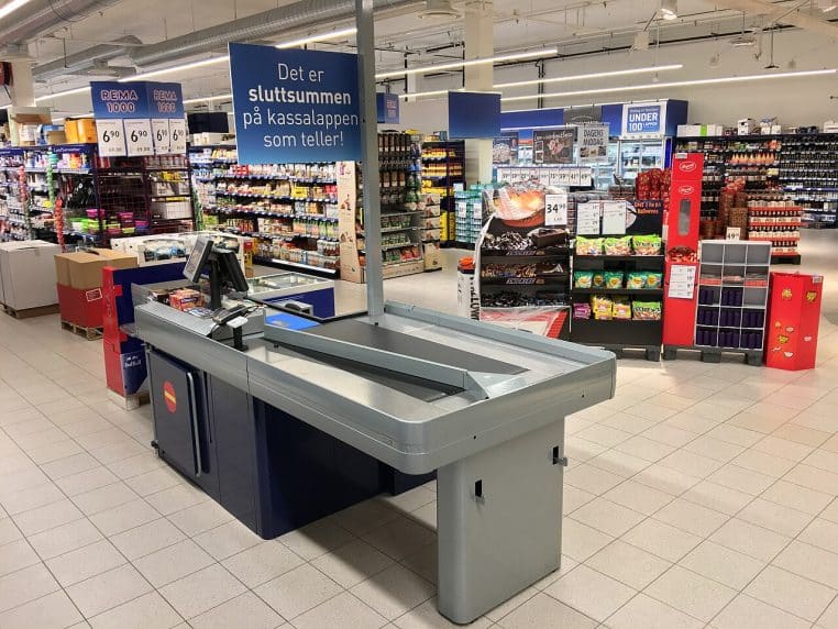 Poste de caisse vide dans un supermarché, tapis roulant et rayons colorés en arrière-plan