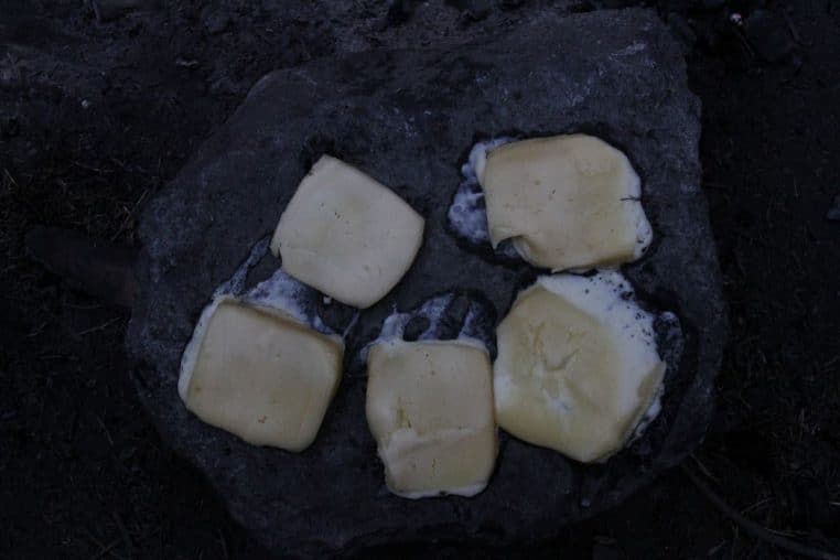 Morceaux de fromage à raclette fondant sur une pierre chauffée, en extérieur, pour une cuisson simple et rustique.
