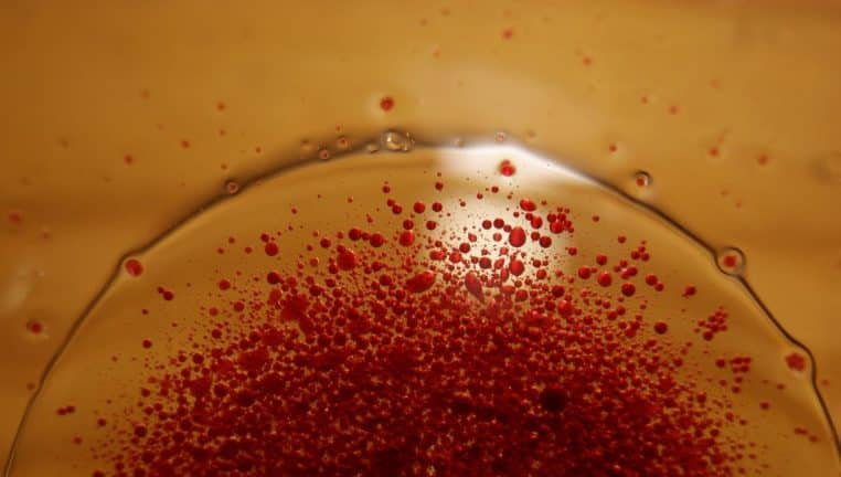 Texture huileuse ambrée avec micro-gouttelettes rouges en suspension, effet sérum en macro, format paysage