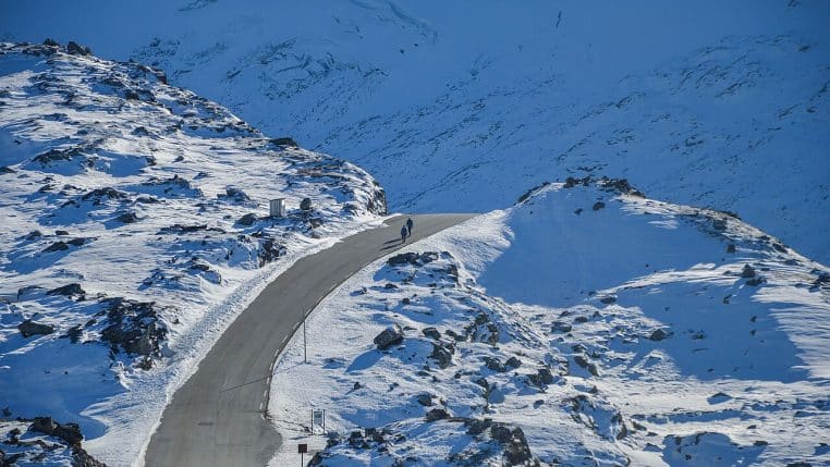 Route dégagée traversant un paysage de montagne entièrement enneigé, avec des silhouettes au loin sur la chaussée.