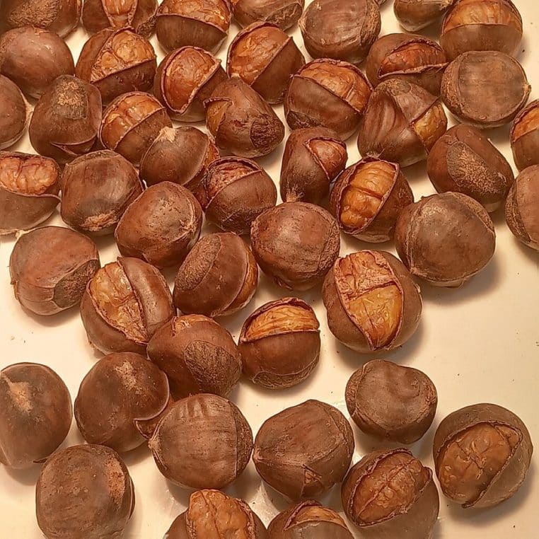 Gros plan sur un tas de châtaignes rôties entières, encore dans leur peau, représentant un encas automnal riche en fibres solubles.